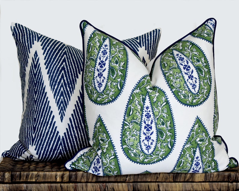 May include: Two decorative throw pillows with a white background. One pillow has a blue and white geometric pattern. The other pillow has a green paisley pattern.