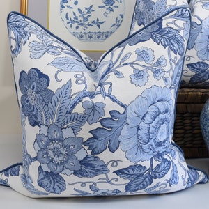 May include: A white cushion with a blue floral pattern. The cushion has a blue border and is made of a soft, comfortable fabric.