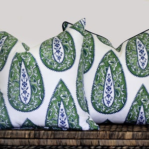 May include: Two decorative throw pillows with a white background and a green and blue paisley pattern. The pillows have black trim.