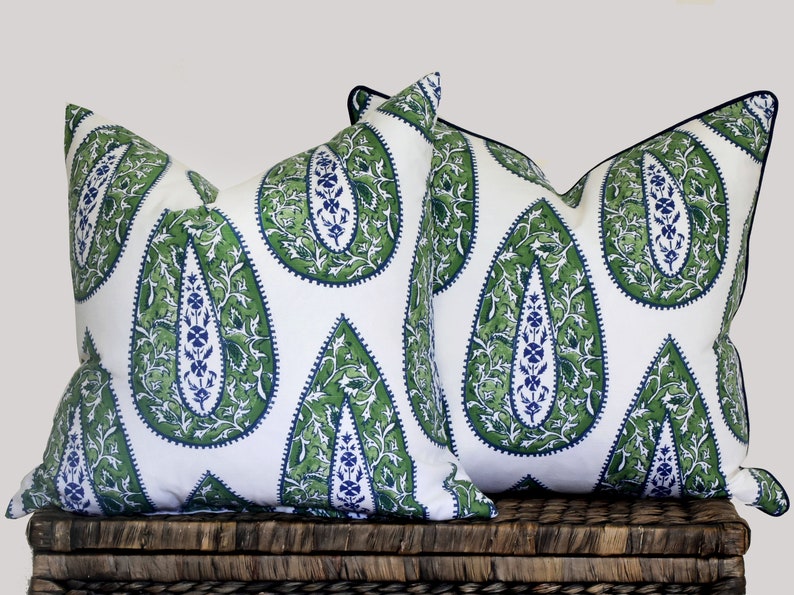 May include: Two decorative throw pillows with a white background and a green and blue paisley pattern. The pillows have black trim.