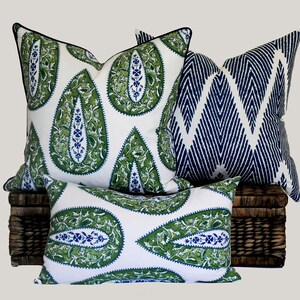 May include: Three decorative throw pillows with a paisley pattern. The pillows are white with green and blue accents. The pillows are arranged on a wicker basket.