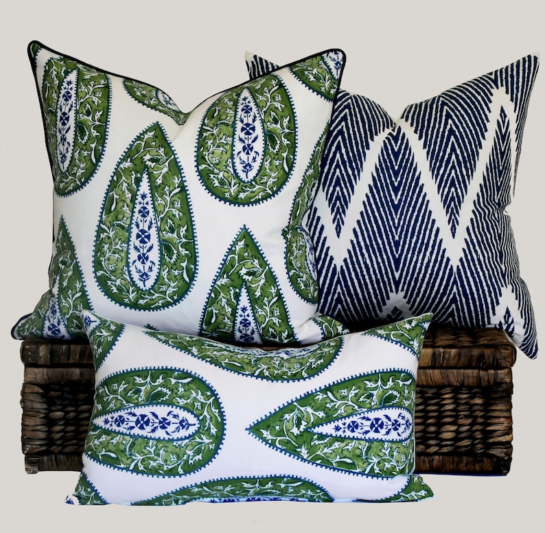 May include: Three decorative throw pillows with a paisley pattern. The pillows are white with green and blue accents. The pillows are arranged on a wicker basket.