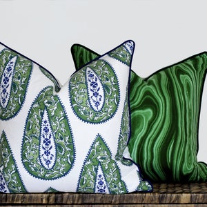 May include: Two decorative throw pillows, one with a green and white paisley pattern and the other with a green marbled pattern. Both pillows have a navy blue trim.
