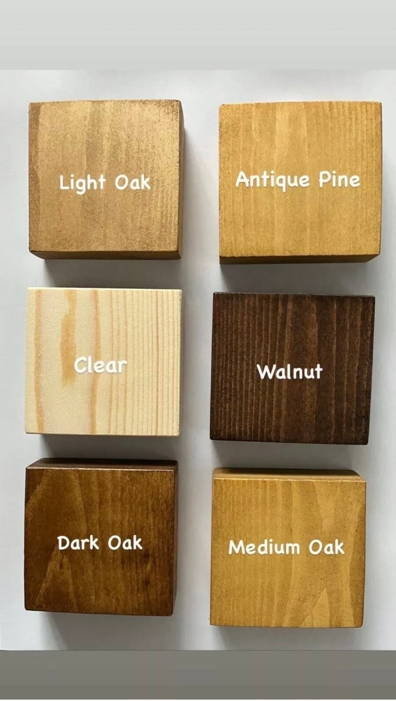 May include: Six square wooden blocks arranged in two columns, each displaying a different wood stain finish with white text labels: Light Oak, Antique Pine, Clear, Walnut, Dark Oak, and Medium Oak. Each block shows natural wood grain patterns.