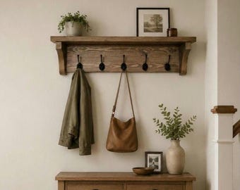 May include: A wall-mounted wooden coat rack with five black metal hooks, featuring a top shelf holding a potted plant and a framed picture. Below, a wooden console table with two drawers holds a small bowl, a framed photo, and a vase with greenery.