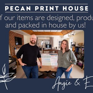 Owners Angie and Eric Stand in their print studio in front a large work table and printers smiling in front of large prints of their continuous and hanging wall calendar prints.