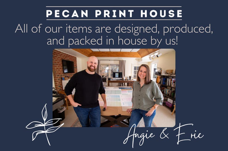 Owners Angie and Eric Stand in their print studio in front a large work table and printers smiling in front of large prints of their continuous and hanging wall calendar prints.