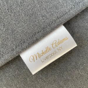 May include: White fabric label with gold text that reads "Michelle Adams, Liverpool, NY".