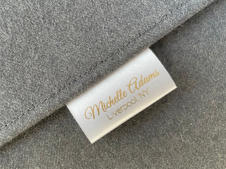 May include: White fabric label with gold text that reads "Michelle Adams, Liverpool, NY".