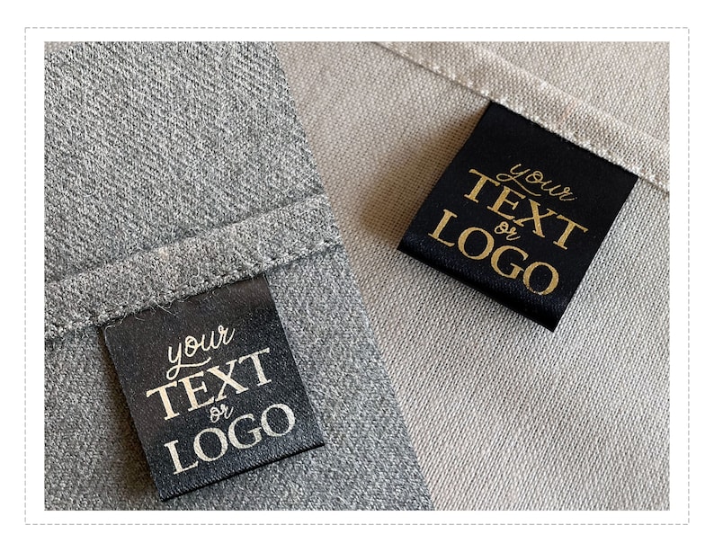 K&ouml;nnte beinhalten: Zwei schwarze Stoff-Etiketten mit goldener Aufschrift "Ihr Text oder Logo" auf einem grauen und beigefarbenen Stoffhintergrund.