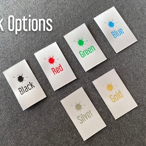 May include: Ink color options for a product, shown on small white fabric swatches. The colors are black, red, green, blue, silver, and gold.