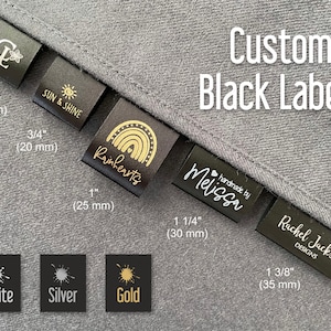 K&ouml;nnte beinhalten: Schwarze Stoff-Etiketten mit goldener Beschriftung in verschiedenen Gr&ouml;&szlig;en. Die Etiketten zeigen verschiedene Designs, darunter ein Sonnen- und Sonnenschein-Design, ein Regenbogen-Design und ein Herz-Design. Die Etiketten werden auf einem grauen Hintergrund mit einem Farbmuster in Wei&szlig;, Silber und Gold gezeigt.