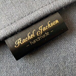K&ouml;nnte beinhalten: Schwarzes Stofflabel mit goldener Beschriftung "Rachel Jackson - handmade -"