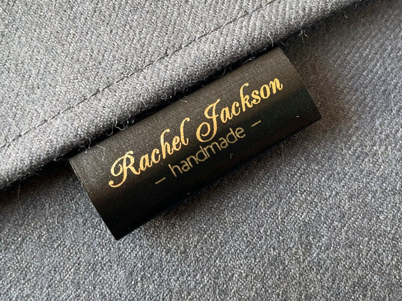 K&ouml;nnte beinhalten: Schwarzes Stofflabel mit goldener Beschriftung "Rachel Jackson - handmade -"
