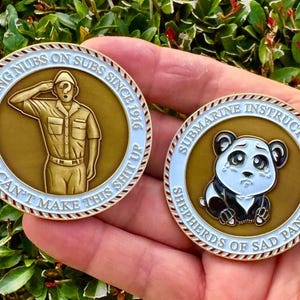 May include: Two gold-colored challenge coins. The first coin features a cartoon sailor saluting with the text "Putting Nubs on Subs Since 1916 You Can't Make This Shit Up". The second coin features a cartoon panda with the text "Submarine Instructors Shepherds of Sad Pandas".