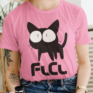 Puede incluir: Camiseta rosa con un gato de dibujos animados negro con ojos grandes y el texto "FLCL" impreso en la parte delantera.