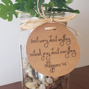 May include: A mason jar filled with small stones and topped with a green plant. A brown tag with the text "Don't worry about anything, instead, pray about everything. Philippians 4:6" is tied around the jar with a brown ribbon.