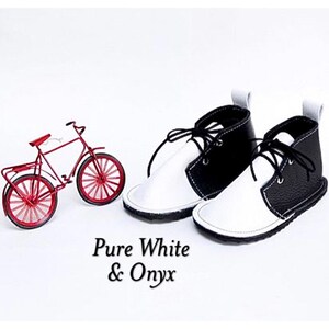 May include: A pair of black and white leather baby shoes with laces. The shoes are called "Pure White & Onyx".