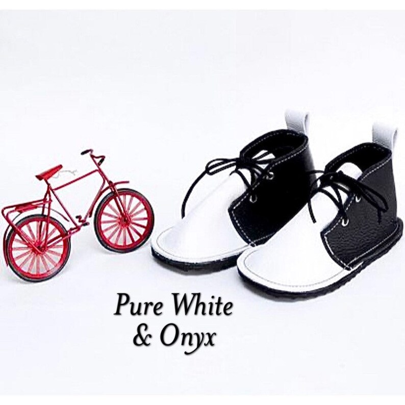 May include: A pair of black and white leather baby shoes with laces. The shoes are called "Pure White & Onyx".