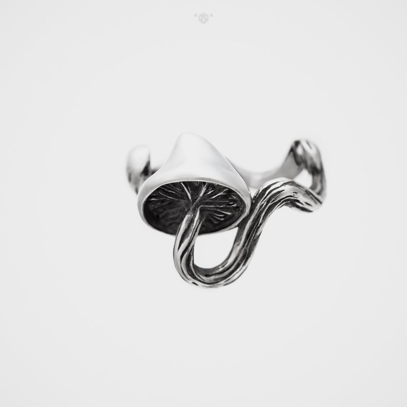 May include: A silver ring featuring a detailed mushroom design with a curved stem and a cap.
