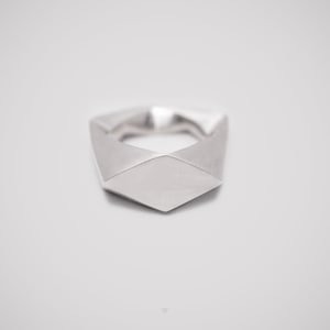 May include: A silver ring with a geometric design. The ring is made of a single piece of metal and has a smooth, polished finish.