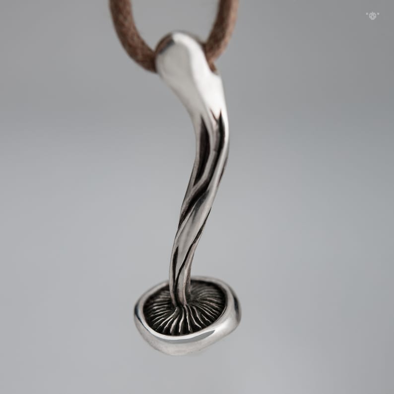 May include: A silver mushroom pendant necklace with a detailed stem and cap. The pendant is attached to a brown leather cord.