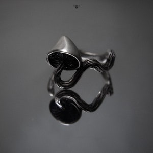 May include: A silver ring with a mushroom design. The mushroom is on a branch that wraps around the ring.