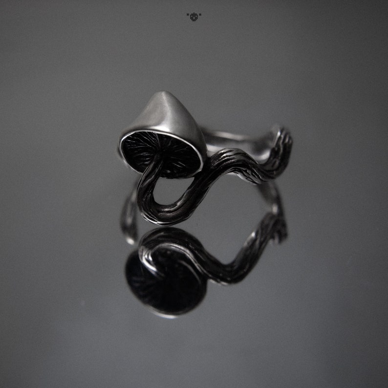 May include: A silver ring with a mushroom design. The mushroom is on a branch that wraps around the ring.