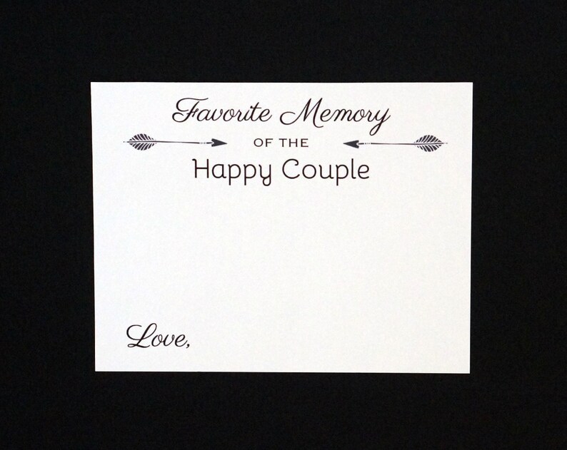 May include: A white card with the text "Favorite Memory of the Happy Couple" in a decorative font, with arrow accents. The word "Love," is written at the bottom. The card is set against a black background.