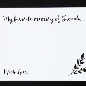 May include: A white card with black calligraphy that reads "My favorite memory of Jacinda..." and "With Love,". A black leaf design is in the bottom right corner. The card is on a black background.