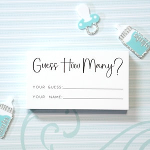 Op de afbeelding: Een witte kaart met de tekst "Guess How Many?" in zwart script, met ruimte voor "Your Guess" en "Your Name". De kaart is omgeven door baby-thema decoraties, waaronder een fopspeen en babyflessen in blauwe en zilveren tinten.