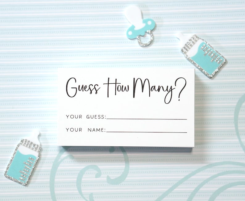 Op de afbeelding: Een witte kaart met de tekst "Guess How Many?" in zwart script, met ruimte voor "Your Guess" en "Your Name". De kaart is omgeven door baby-thema decoraties, waaronder een fopspeen en babyflessen in blauwe en zilveren tinten.