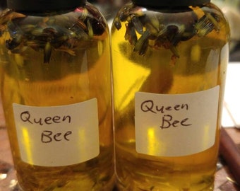 Peut inclure: Deux petites bouteilles en verre remplies d'un liquide jaune et d'herbes séchées. Les deux bouteilles ont un bouchon noir et une étiquette blanche sur laquelle est inscrit "Queen Bee".