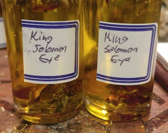 Peut inclure: Deux petites bouteilles en verre avec des bouchons noirs remplies d'un liquide jaune et de diverses herbes et fleurs. Les bouteilles portent des étiquettes bleues et blanches sur lesquelles est inscrit "King Solomon Eye".