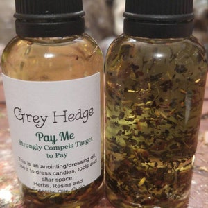以下が含まれることがあります： 透明な液体とハーブが入った小さなガラス瓶が2本。前の瓶のラベルには、「Grey Hedge Pay Me Strongly Compels Target to Pay This is an anointing/dressing oil. Use it to dress candles, tools and altar space. Herbs, Resins and Essential Oils」と書いてあります。