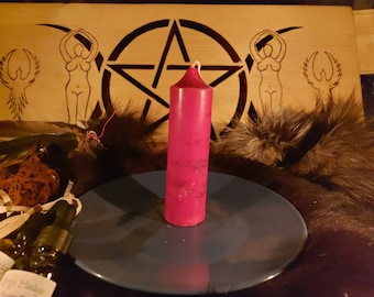 May include: A red pillar candle on a blue plate with a wooden background featuring a pentagram and two figures. There are two bottles of essential oil in the foreground.