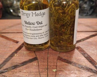 May include: Two small glass bottles with black lids filled with a yellow liquid and herbs. The bottles have labels that read "Grey Hedge" and "Mellow Out". The text on the label describes the oil as an anointing/dressing oil.