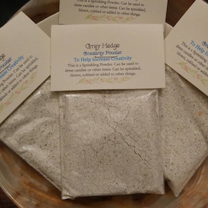 May include: Two white paper bags filled with a white powder. The bags have labels that read "Grey Hedge Creativity Powder To Help Increase Creativity. This is a Sprinkling Powder. Can be used to dress candles or other items. Can be sprinkled, blown, rubbed or added to other things."