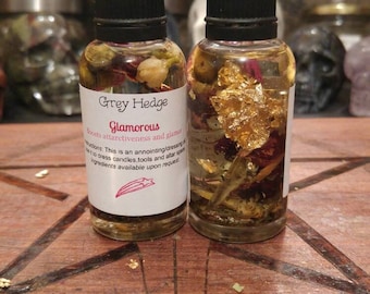 Peut inclure: Deux petites bouteilles en verre avec des bouchons noirs remplies d'un liquide clair et de diverses plantes, y compris des fleurs séchées et des paillettes d'or. Les bouteilles portent des étiquettes qui indiquent "Grey Hedge" et "Glamorous Boosts attractiveness and glamor Instructions. This is an annointing/dressing oil to dress candles, tools and altar spaces. Ingredients available upon request."
