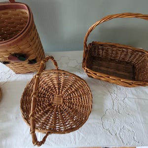 Puede incluir: Cuatro cestas de mimbre tejidas de diferentes formas y tama&ntilde;os. Las cestas est&aacute;n hechas de mimbre marr&oacute;n natural y tienen asas. Las cestas est&aacute;n sobre un mantel blanco.