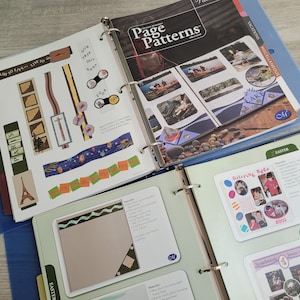 May include: Open binders with scrapbook pages. One binder displays the text "Page Patterns" and images of kayaking. Another binder shows travel-themed scrapbook elements, including the Eiffel Tower and the word "PARIS".