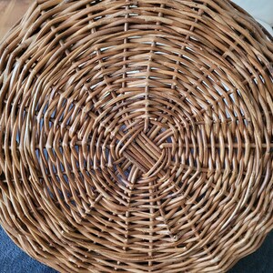 May include: A round, woven wicker basket with a natural brown color. The basket is made of tightly woven strips of wicker, creating a smooth, even surface.