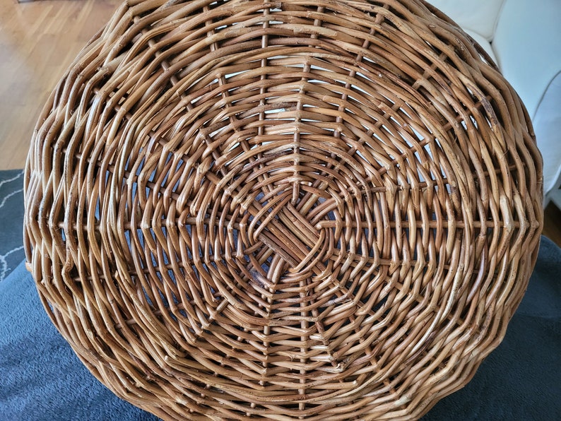 May include: A round, woven wicker basket with a natural brown color. The basket is made of tightly woven strips of wicker, creating a smooth, even surface.