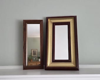 May include: Two rectangular mirrors with brown wooden frames. One mirror has a simple frame, while the other features a gold-colored inner frame. Both mirrors are leaning against a light green wall.