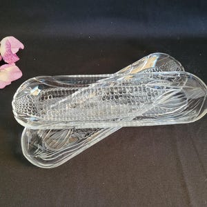 May include: Two clear glass corn on the cob serving dishes. The dishes are shaped like corn on the cob and have a textured surface.