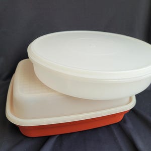 May include: A white plastic storage container with a red base and a matching lid. The container is square and the lid is round.