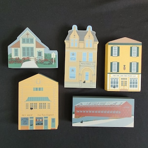 May include: Set of five wooden miniature buildings, painted in various colors, depicting a pet shop, a police station, a covered bridge, a general store, and a shop called "The Owl and the Pussy Cat".