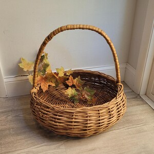 May include: A large, round wicker basket with a woven handle. The basket is filled with dried fall leaves and berries.