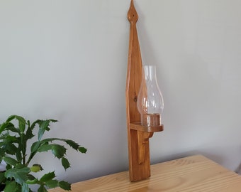 Puede incluir: Un portavelas de pared de madera con una pantalla de vidrio transparente. El soporte está teñido de un color marrón claro y tiene un diseño simple y tradicional.
