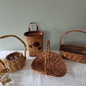 Puede incluir: Cuatro cestas de mimbre tejidas en diferentes formas y tama&ntilde;os. Las cestas est&aacute;n hechas de mimbre marr&oacute;n natural y tienen asas.